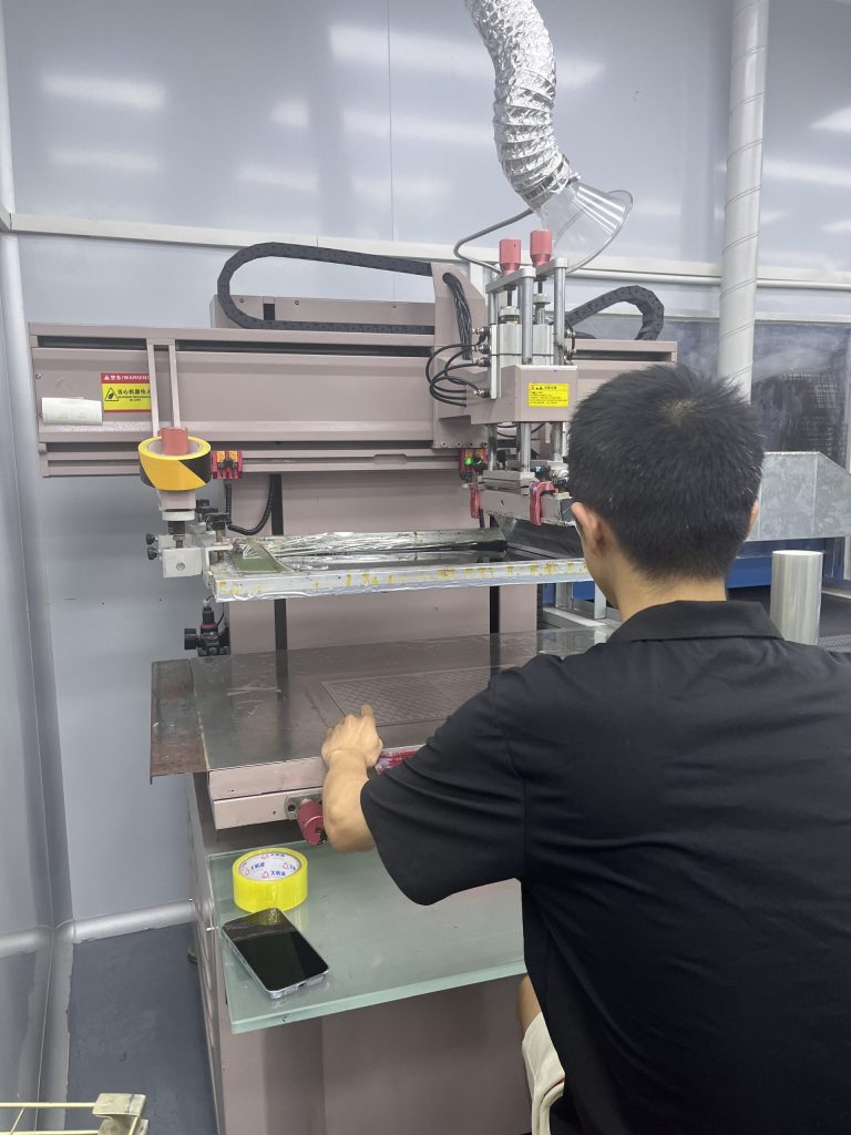 Technician operating a screen printing press for custom PC and PET graphic overlays